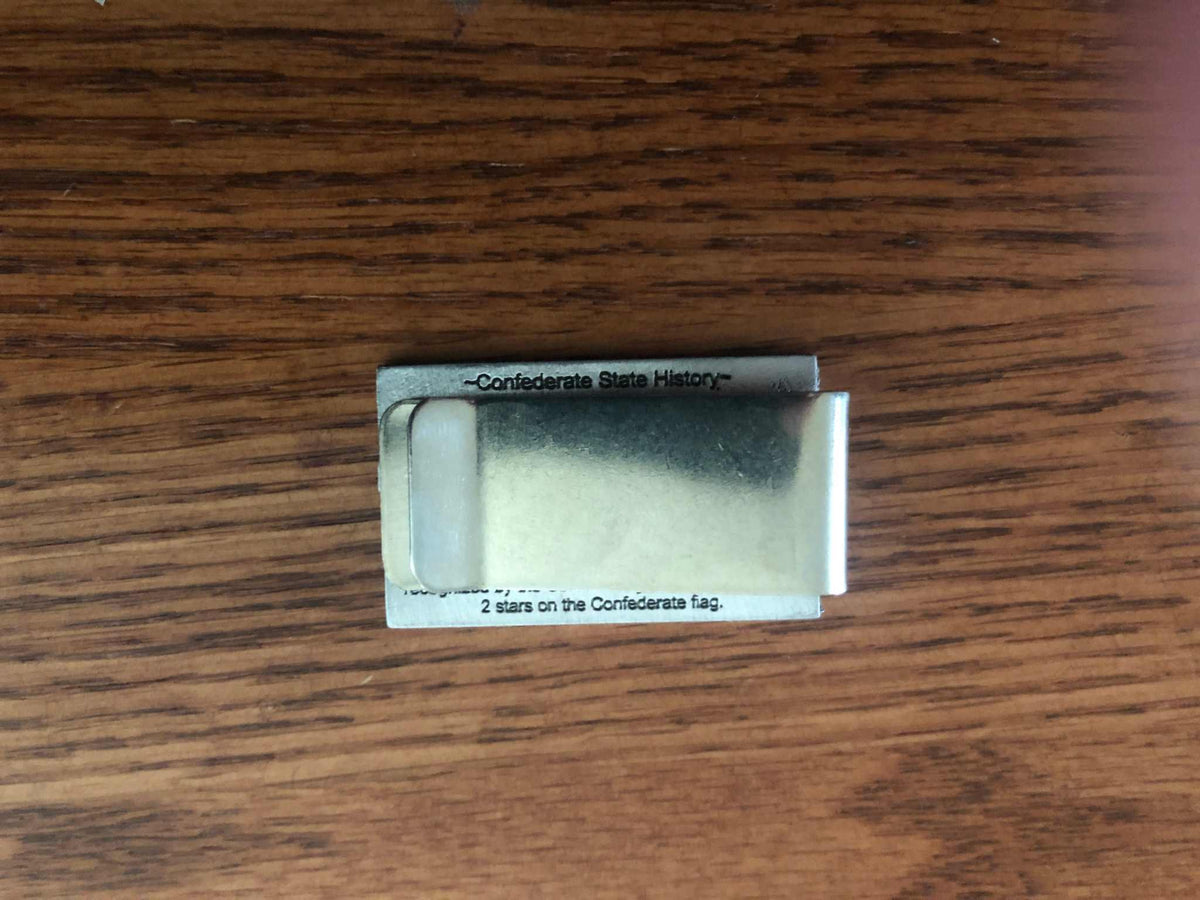 Old Mississippi State Flag Money Clip A silver metal money clip with printed text on its sides, resting on a brown wooden surface.
